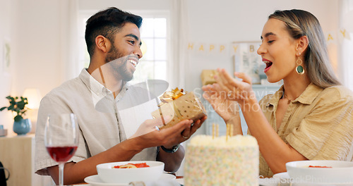 Image of Interracial, couple and celebrate for birthday with gift, being happy and relax together at party. Romance, man and woman with present, bonding and smile in home in living room for hug and embrace.