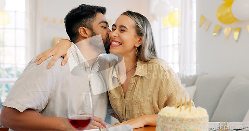 Image of Interracial couple, gift and celebrate birthday being happy, kiss and smile in home at table with cake. Love, man and woman being content, romantic and present being cheerful celebration together.