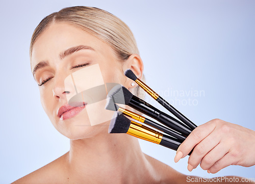 Image of Eyes closed, face and makeup of woman with brushes in studio isolated on a blue background. Facial cosmetics, beauty skincare and female model with tools to apply foundation or powder for aesthetics.