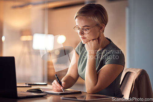 Image of Business woman, book or writing in night office for company planning, schedule or ideas management. Serious, corporate or worker with notebook pen, laptop technology or project agenda of evening task