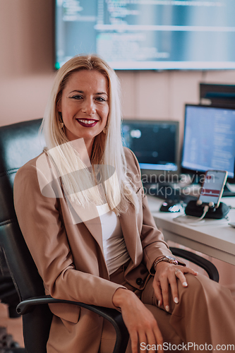 Image of A businesswoman sitting in a programmer's office surrounded by computers, showing her expertise and dedication to technology.