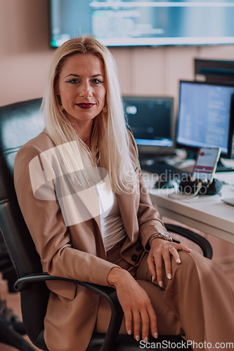 Image of A businesswoman sitting in a programmer's office surrounded by computers, showing her expertise and dedication to technology.