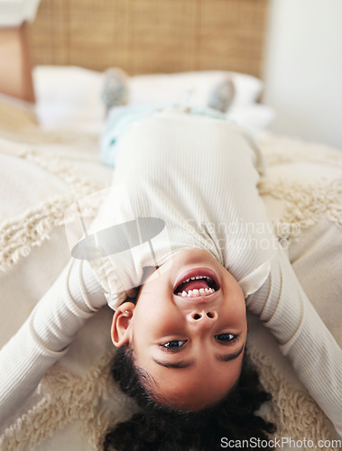 Image of Portrait, child laughing and upside down on bed in bedroom home, having fun and smiling. Comic, smile and happy kid or girl laugh at funny joke, comedy or humor while relaxing and enjoying time alone