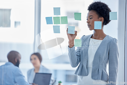 Image of Black woman, writing and schedule for team planning or brainstorming tasks on glass board at the office. Serious African American female working on project plan, with sticky note for strategy