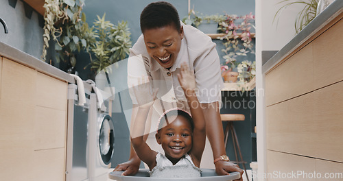 Image of Playful black mother pushing her daughter around in a laundry basket at home. Young woman and her child playing and having fun while spending time at home