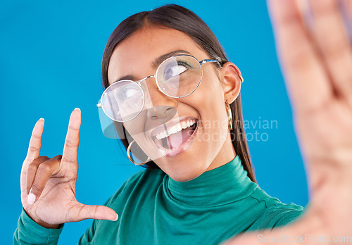 Image of Woman, face and fashion selfie with rock on hand for gen z attitude on a blue background with glasses. Happy model person in studio with excited and cool hand sign or emoji with beauty and motivation