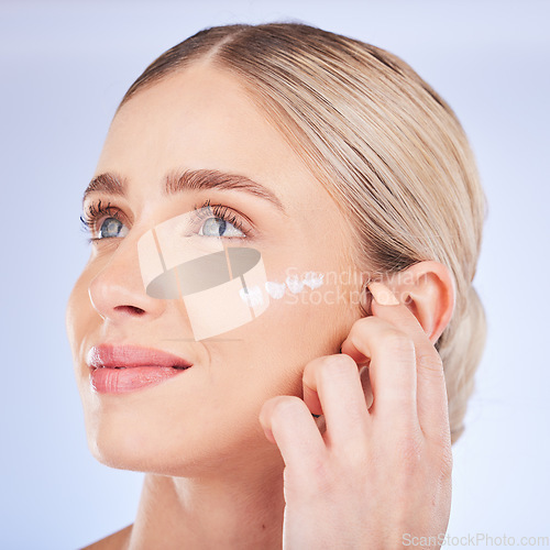 Image of Beauty, face skincare and woman with cream in studio isolated on a blue background. Dermatology cosmetics, thinking and happy female model apply lotion, creme or moisturizer product for healthy skin.