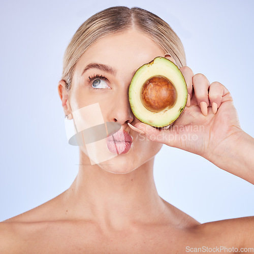 Image of Skincare, face and woman with avocado in studio isolated on a blue background. Cosmetics kiss, fruit and thinking female model with food for omega 3, nutrition or diet, healthy skin or beauty pout.