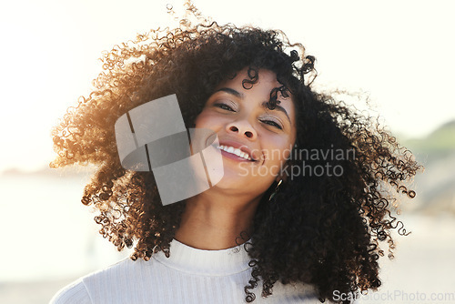 Image of Black woman, afro and wind in hair outdoor with a smile and portrait at beach for vacation or freedom. Face of happy young model person in nature for peace, travel and time to relax on sunset holiday