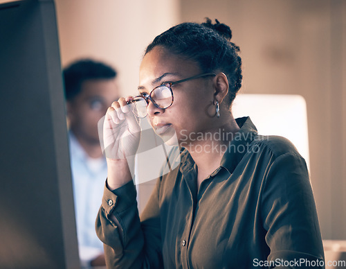 Image of Serious black woman, computer and reading email, code or corporate information at night by the office. African American female employee focusing with glasses on PC working late at the workplace