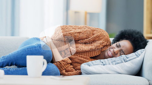 Image of Woman with menstruation stomach cramps and belly ache holding her sore tummy while feeling ill on a sofa at home. Hungry female with period getting sick, bloated and uncomfortable with digestive pain
