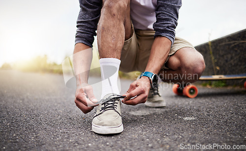 Image of Hands, shoes and skate with a man tying his laces while on an asphalt skateboard for fun or recreation. Road, training or footwear with a male skater outdoor on a street while fastening his shoelaces