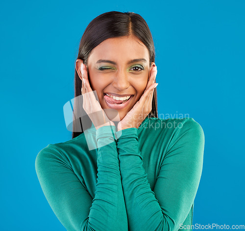 Image of Black woman, studio portrait and wink with tongue, smile and makeup for beauty, aesthetic and blue background. Gen z model, funny face and comic with hands on ears, happy and cosmetics with fashion