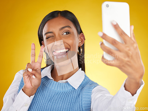 Image of Selfie, face and peace with a woman in studio on a yellow background to post a profile picture update. Phone, social media and hand gesture with an attractive young female posing for a photograph