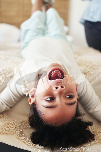 Image of Children, fun and bed with a black girl playing upside down in a bedroom of her home looking excited. Kids, happy and playful with a young female child shouting or screaming while lying in a house