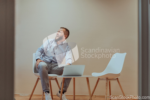 Image of A confident businessman sitting and using laptop with a determined expression, while a beige background enhances the professional atmosphere, showcasing his productivity and expertise.