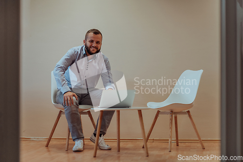 Image of A confident businessman sitting and using laptop with a determined expression, while a beige background enhances the professional atmosphere, showcasing his productivity and expertise.