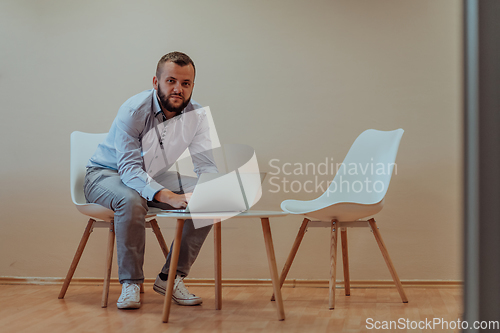 Image of A confident businessman sitting and using laptop with a determined expression, while a beige background enhances the professional atmosphere, showcasing his productivity and expertise.