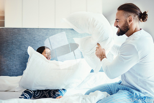 Image of Happy, love and father in pillow fight with his child on the bed in the bedroom of family house. Happiness, smile and dad being playful with his boy kid while bonding, playing and having fun at home.