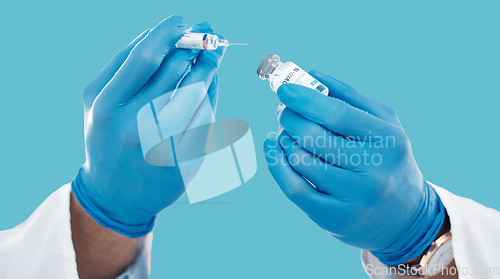 Image of Closeup, hands and needle for vaccine, healthcare and research with blue studio background. Zoom, gloves and liquid bottle with medical equipment, medicine and vial for cure, vaccination and results