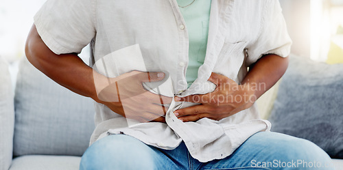 Image of Man on a sofa with a tummy ache, pain or sickness while relaxing in the living room of his home. Illness, medical emergency and male with diarrhea, food poisoning or indigestion rubbing his stomach.
