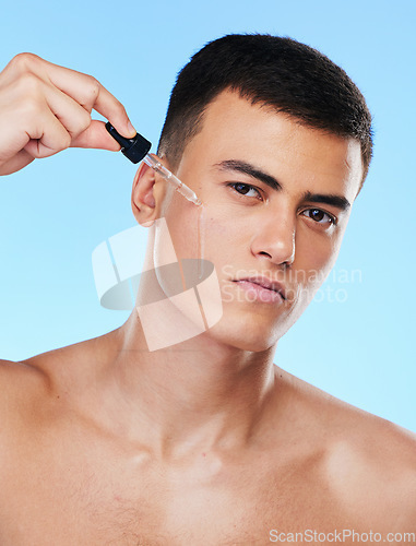 Image of Man, serum and drop for face in studio with beauty, wellness and facial change by blue background. Young model, oil or hyaluronic acid for glow, shine and cleaning skin with cosmetic transformation