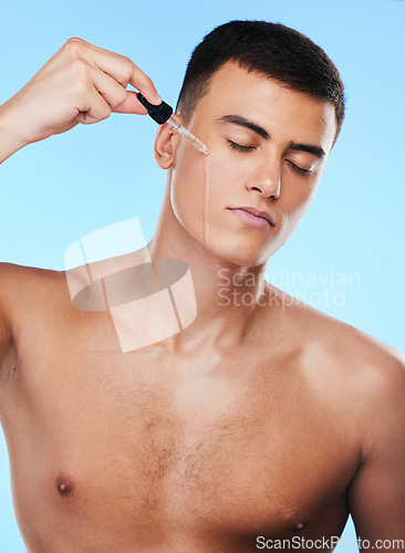 Image of Man, skincare serum and drop in studio with beauty, wellness and facial change by blue background. Young model, oil or hyaluronic acid for glow, shine and cleaning face with cosmetic transformation