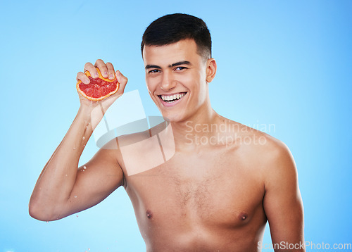 Image of Smile, grapefruit and squeeze with portrait of man in studio for health, detox or natural cosmetics. Vitamin c, nutrition and skincare with person and fruit on blue background for self care and glow