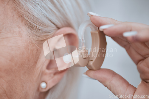 Image of Hand, closeup and hearing aid in ear for old woman, audio or sound for listening, healthcare or retirement. Senior lady, deaf or person with disability holding technology for ear implant for wellness