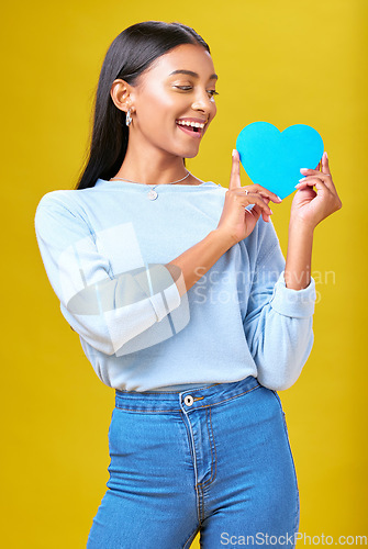 Image of Donation, smile and woman with blue heart in studio for help, hope or empathy on yellow background. Charity, lady or social media poster for thank you, support for autism or people with a disability