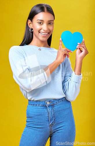 Image of Portrait, smile and woman with blue heart in studio with help, hope or empathy on yellow background. Face, girl and social media icon for thank you, support and trust or people with loyalty to peace