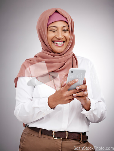 Image of Smile, phone and mature muslim woman in a studio scroll on social media, mobile app or the internet. Happy, religion and islamic female model with a hijab browsing on a cellphone by a gray background