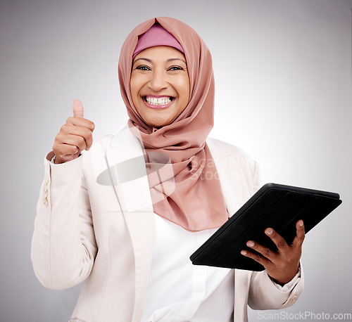 Image of Thumbs up, tablet and portrait of an islamic woman in studio doing research on the internet. Happy, smile and mature muslim female model with technology and agreement hand gesture by gray background.