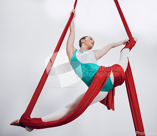 Image of Flexibility, aerial silk and acrobat woman in air for performance, sports and balance. Gymnastics, athlete person or gymnast hanging on red fabric and white background with space, art and creativity