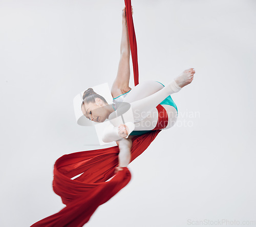 Image of Acrobat, gymnastic and aerial silk with a woman in air for performance, sports and balance. Young athlete person or gymnast hanging on red fabric and white background with space, art and creativity