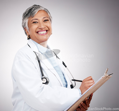 Image of Woman, portrait and doctor writing on clipboard in studio for notes, healthcare administration or info. Happy mature surgeon with report of insurance checklist, documents or script on gray background