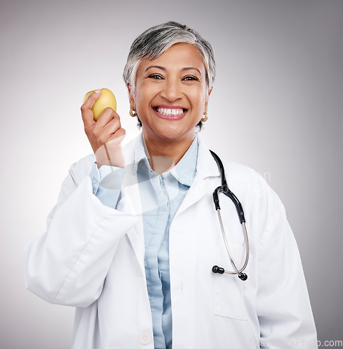 Image of Doctor, woman and portrait with apple in studio for vitamin c benefits, detox and dietician on gray background. Happy mature nutritionist with fresh fruits for nutrition, healthy food and wellness