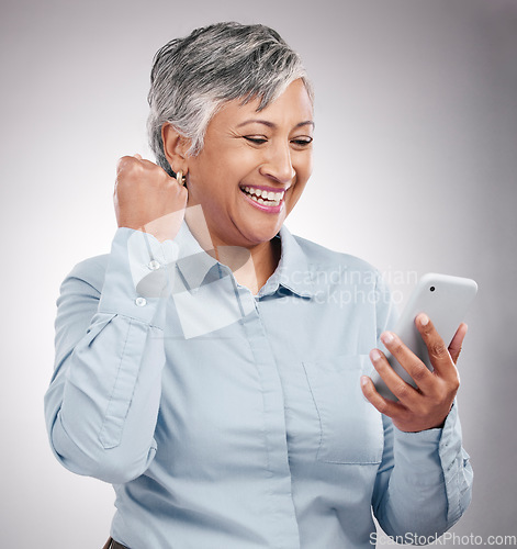 Image of Celebration, phone and senior woman in studio winning an online bet, good news or prize. Happy, fist pump and elderly female model cheering with cellphone for success isolated by gray background.