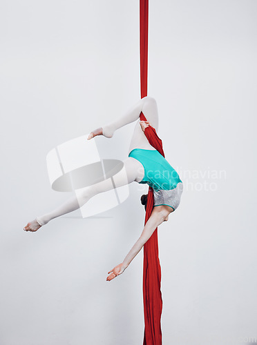 Image of Aerial silk, acrobat and gymnastics with a woman in air for performance, sports and balance. Young athlete person or gymnast hanging on red fabric and white background with space, art and creativity