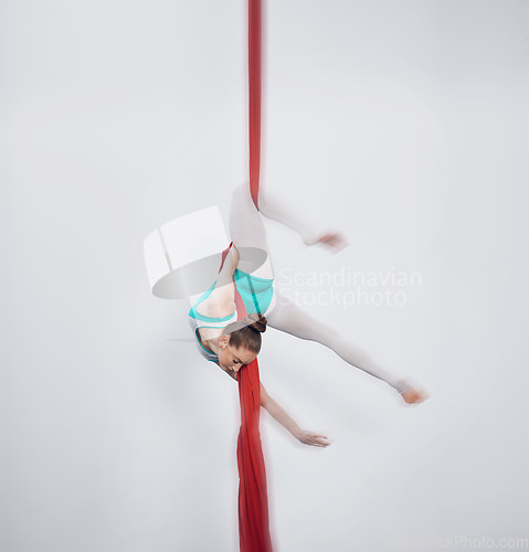 Image of Gymnastics, acrobat and aerial silk with a sports woman in air for performance and balance. Young athlete person or gymnast hanging on red fabric and white background with space, art and creativity