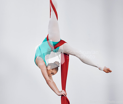 Image of Gymnastics, aerial acrobat and a woman in air for silk performance, sports and balance. Athlete person, gymnast or dancer hanging on red fabric and white background for space, art and creativity