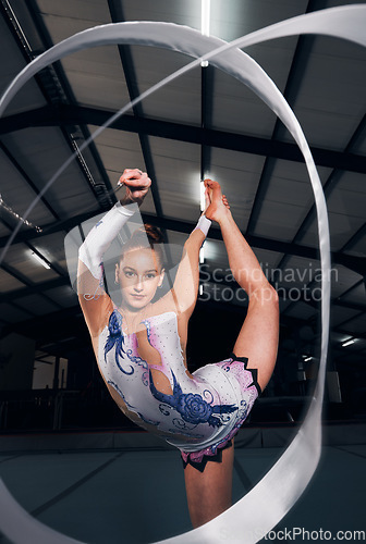 Image of Woman, portrait and balance for ribbon gymnastics in competition, performance or concert in dark arena. Flexible dancer, rhythm and agile athlete training with talent, creative contest or sports show