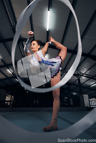 Image of Woman, dancer and balance for ribbon gymnastics in competition, sports performance or concert in dark arena. Flexible athlete, energy and stretching for agile training, challenge or rhythm in contest