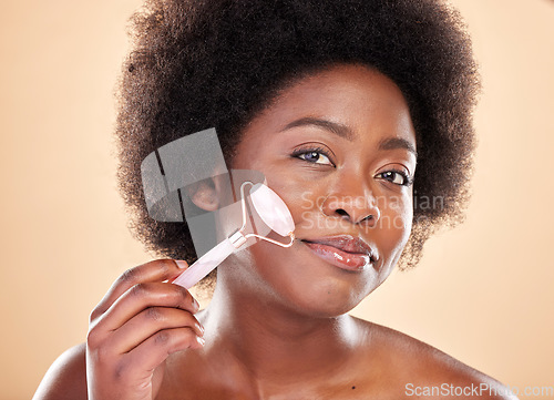 Image of Black woman, face roller and portrait of beauty, rose quartz cosmetics and natural skincare on studio background. Happy model, facial massage and crystal tools for dermatology of lymphatic drainage