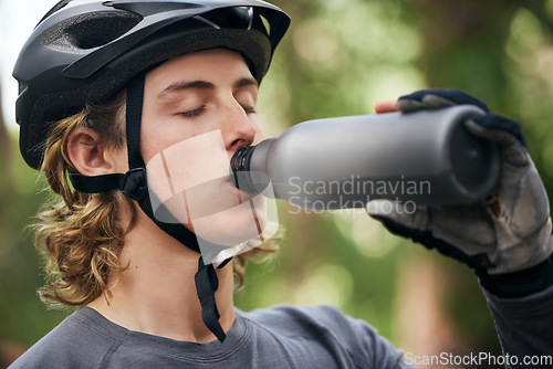 Image of Forest, biker and man with a water bottle, wellness and exercise with workout, refreshing and break. Healthy person, athlete or guy in the woods, hydration and outdoor with liquid, fitness and helmet