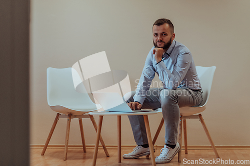 Image of A confident businessman sitting and using laptop with a determined expression, while a beige background enhances the professional atmosphere, showcasing his productivity and expertise.