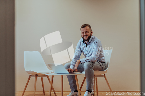 Image of A confident businessman sitting and using laptop with a determined expression, while a beige background enhances the professional atmosphere, showcasing his productivity and expertise.