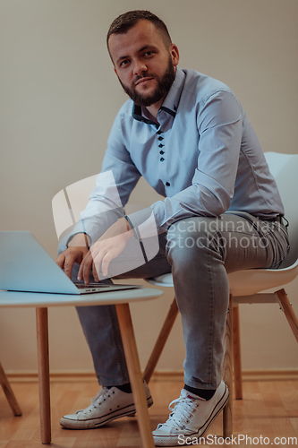 Image of A confident businessman sitting and using laptop with a determined expression, while a beige background enhances the professional atmosphere, showcasing his productivity and expertise.