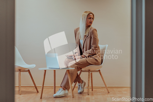 Image of A professional businesswoman sits on a chair, surrounded by a serene beige background, diligently working on her laptop, showcasing dedication and focus in her pursuit of success