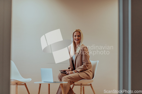 Image of A professional businesswoman sits on a chair, surrounded by a serene beige background, diligently working on her laptop, showcasing dedication and focus in her pursuit of success